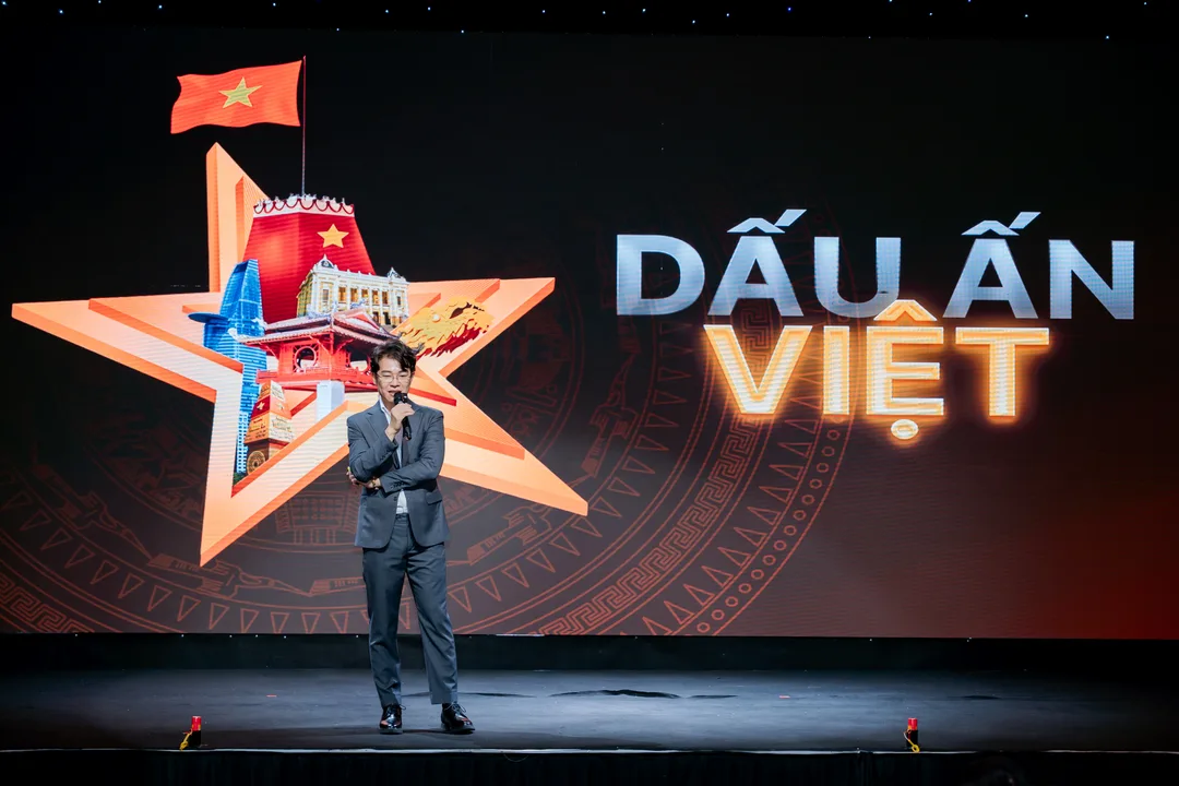 Speaker on stage in front of a red star emblem with the Vietnamese flag and a glowing 'DẤU ẤN VIỆT' (Vietnamese Imprint) event backdrop